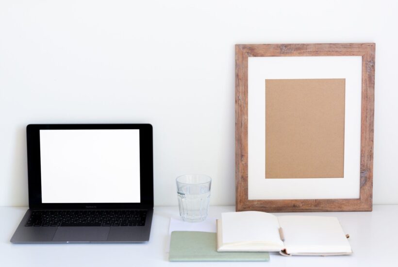 composition of netbook and frame near white organizer and glass of water on table